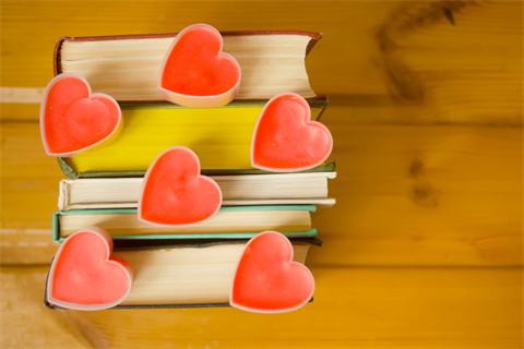 A stack of books has heart-shaped candles resting on the top.